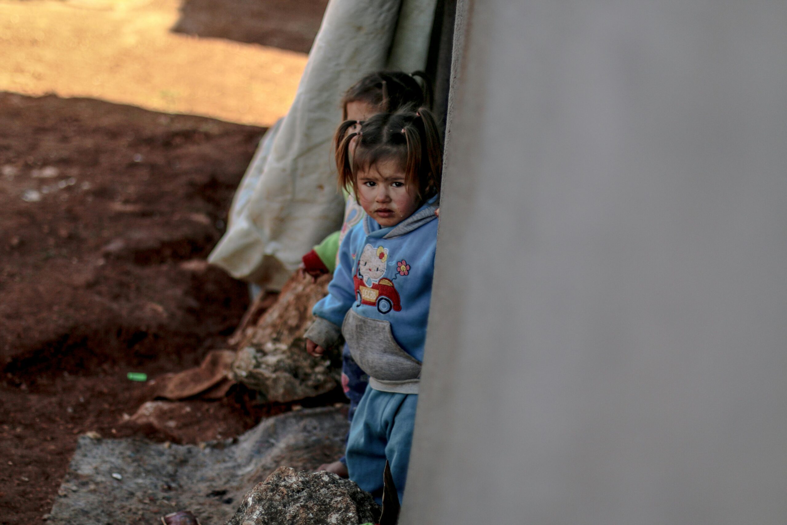 Children stand near a tent in a refugee camp in Idlib, Syria, reflecting resilience and hardship.